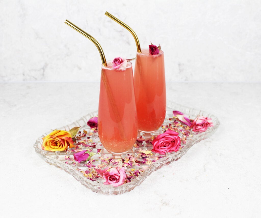 2 glasses of pink lemonade sitting on a glass tray garnished with died rose petals