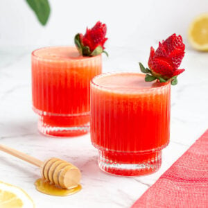 two glasses of strawberry lemonade garnished with roses made from strawberries