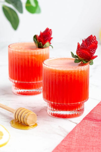 two glasses of strawberry lemonade garnished with roses made from strawberries