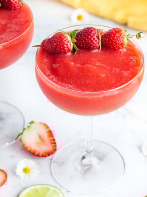 red frozen drink in a coupe glass with 3 strawberries to garnish