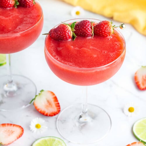 red frozen drink in a coupe glass with 3 strawberries to garnish