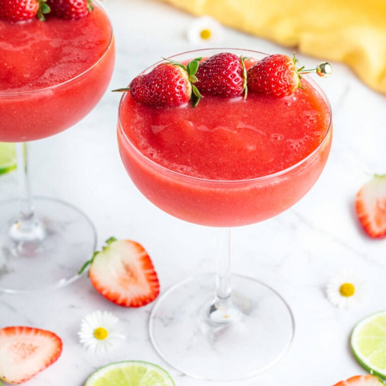 red frozen drink in a coupe glass with 3 strawberries to garnish
