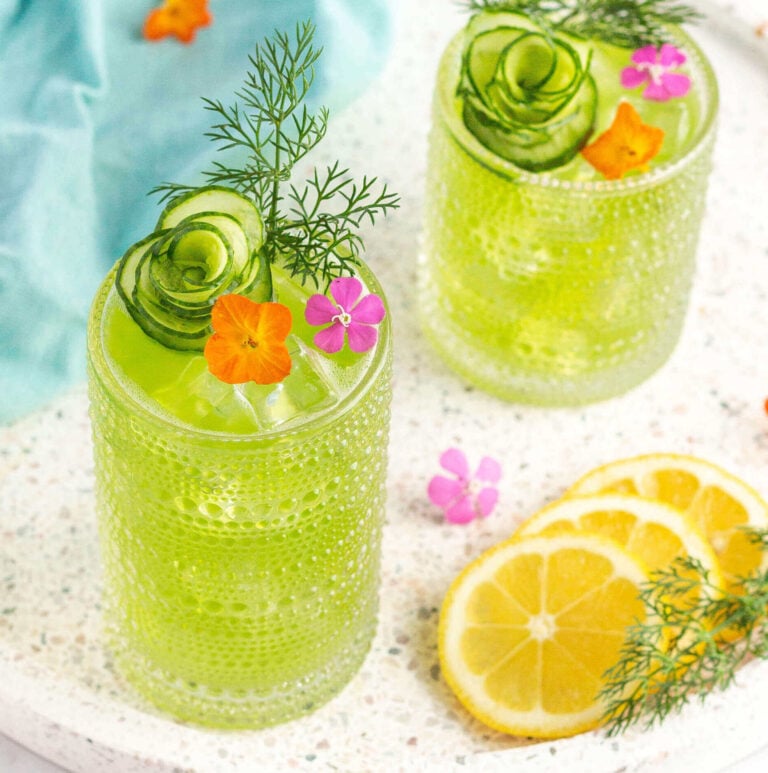 2 green drinks in tall glasses garnished with an orange and pink flower and a sprig of dill
