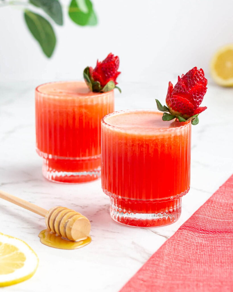 two short glasses of strawberry lemonade garnished with strawberries cut into the shape of roses