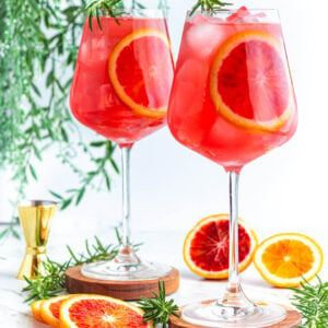 red mocktail in large wine glass with a blood orange round inside and rosemary on top