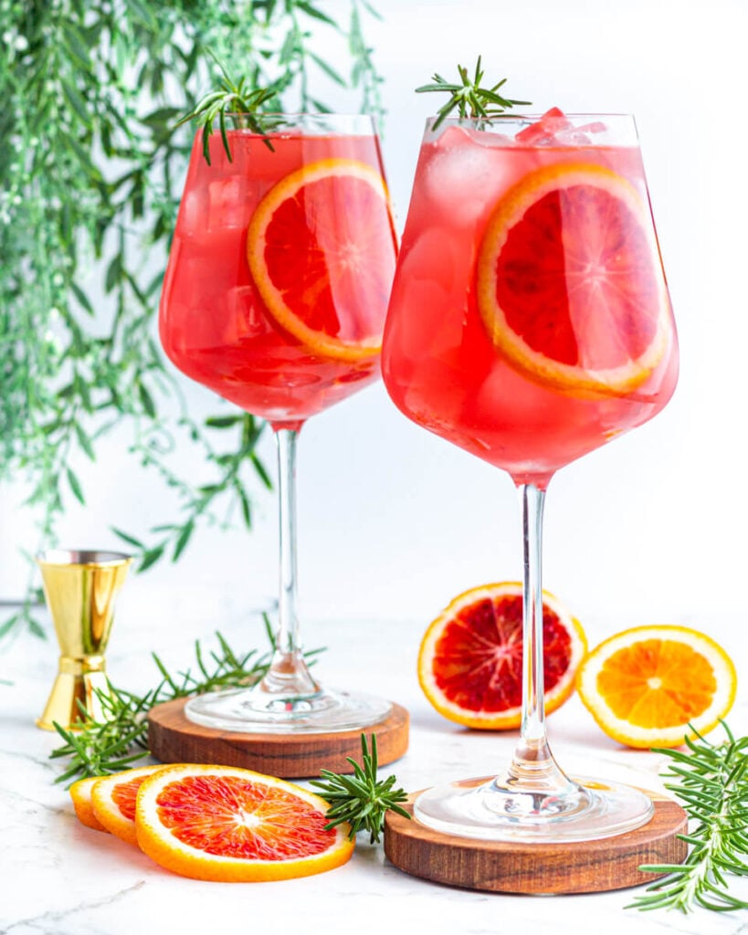 red mocktail in large wine glass with a blood orange round inside and rosemary on top