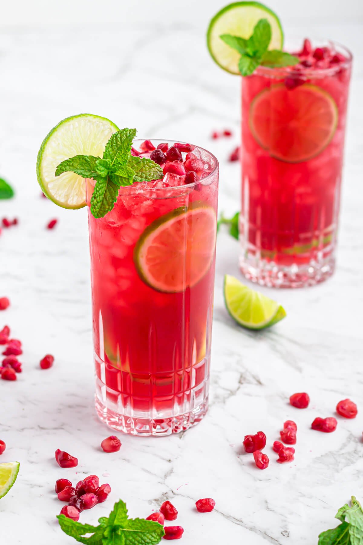 pomegranate mocktail in a tall glass garnished with mint, lime and pomegranate arils, with extra arils and lime scattered in the background