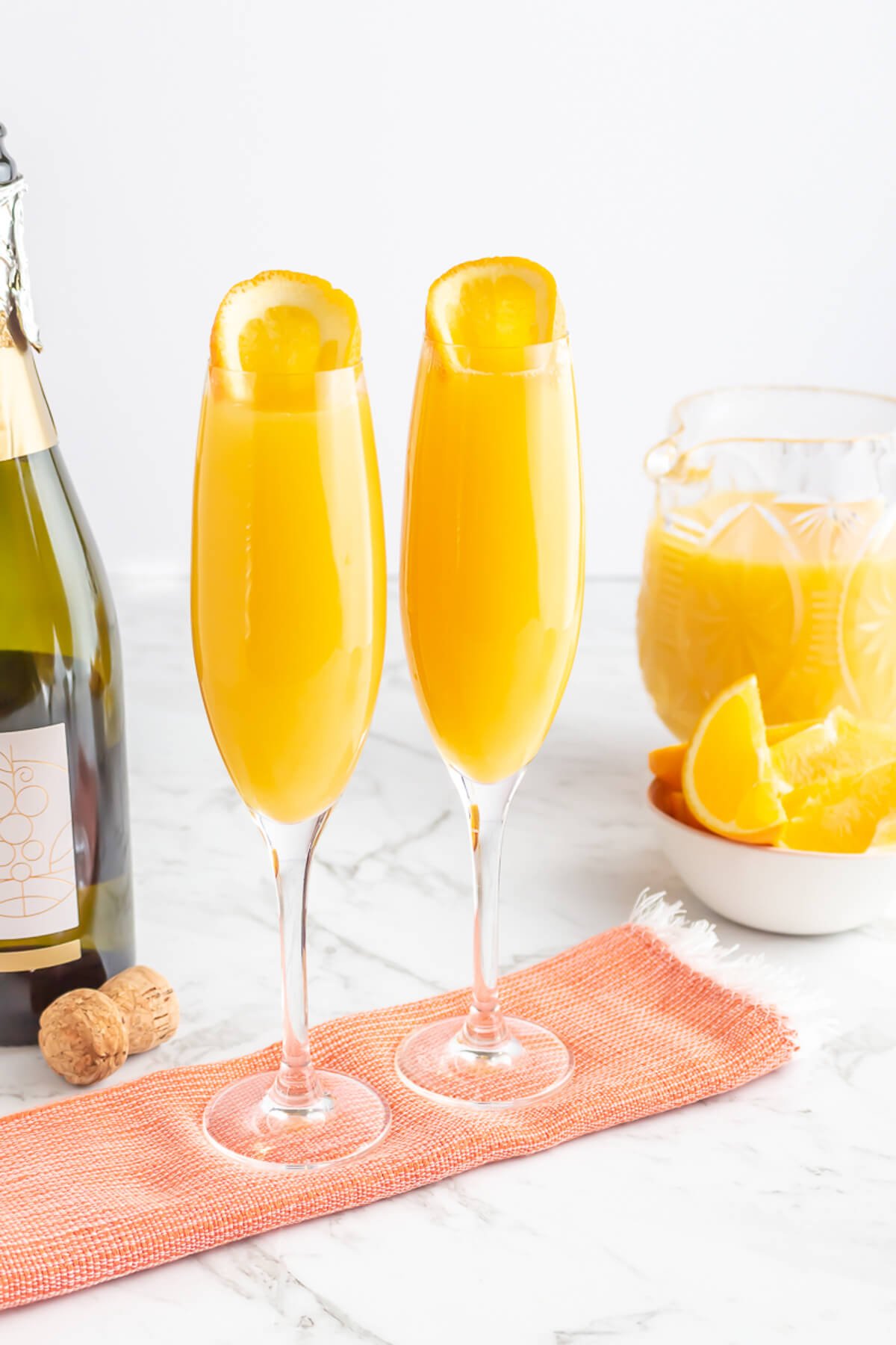 champagne glasses filled with orange liquid and garnished with a round of orange sitting on an orange tea towel.