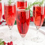 5 red mimosa drinks in champagne flutes garnished with a sprig of rosemary
