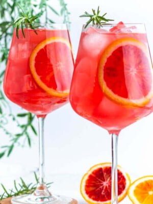 2 wine glasses filled with red liquid and garnished with blood orange slices and rosemary.