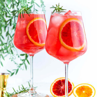 2 wine glasses filled with red liquid and garnished with blood orange slices and rosemary.