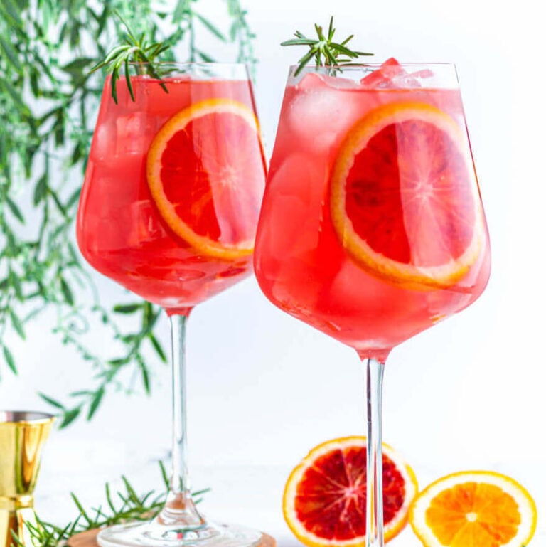 2 wine glasses filled with red liquid and garnished with blood orange slices and rosemary.