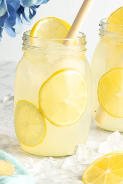 2 jars of yellow ginger lemonade with sliced lemon inside and a bamboo straw