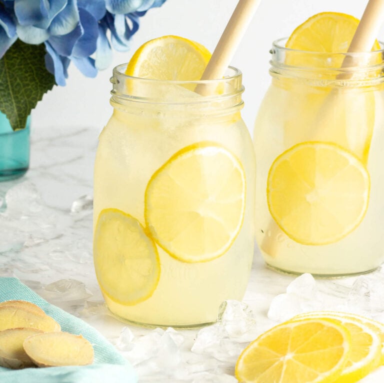 2 jars of yellow ginger lemonade with sliced lemon inside and a bamboo straw