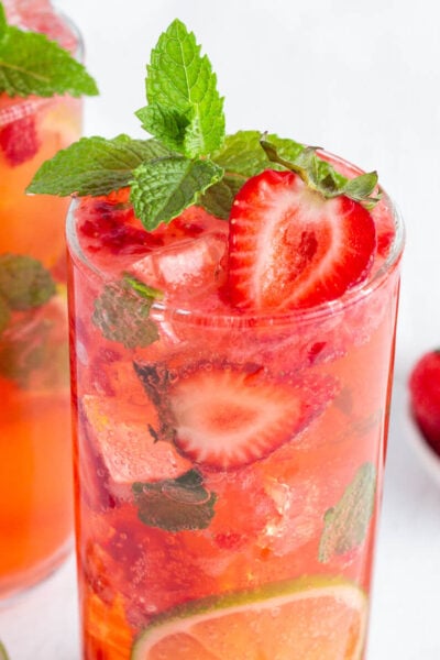 red strawberry mojito mocktail in a tall glass garnished with fresh strawberries, mint and lime rounds