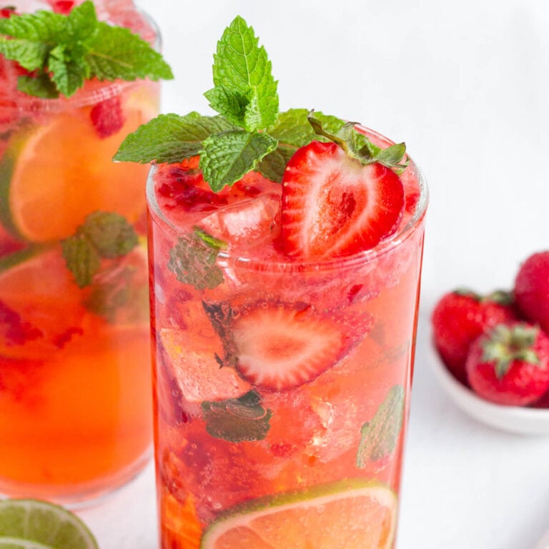 red strawberry mojito mocktail in a tall glass garnished with fresh strawberries, mint and lime rounds