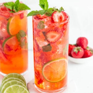 red strawberry mojito mocktail in a tall glass garnished with fresh strawberries, mint and lime rounds