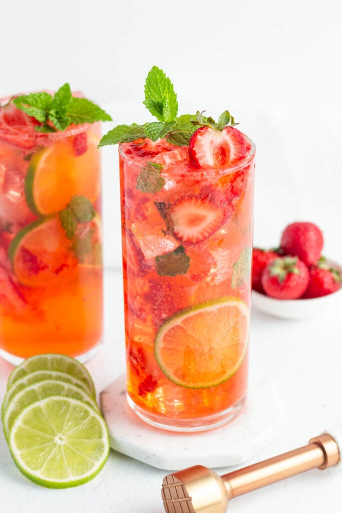 red strawberry mojito mocktail in a tall glass garnished with fresh strawberries, mint and lime rounds