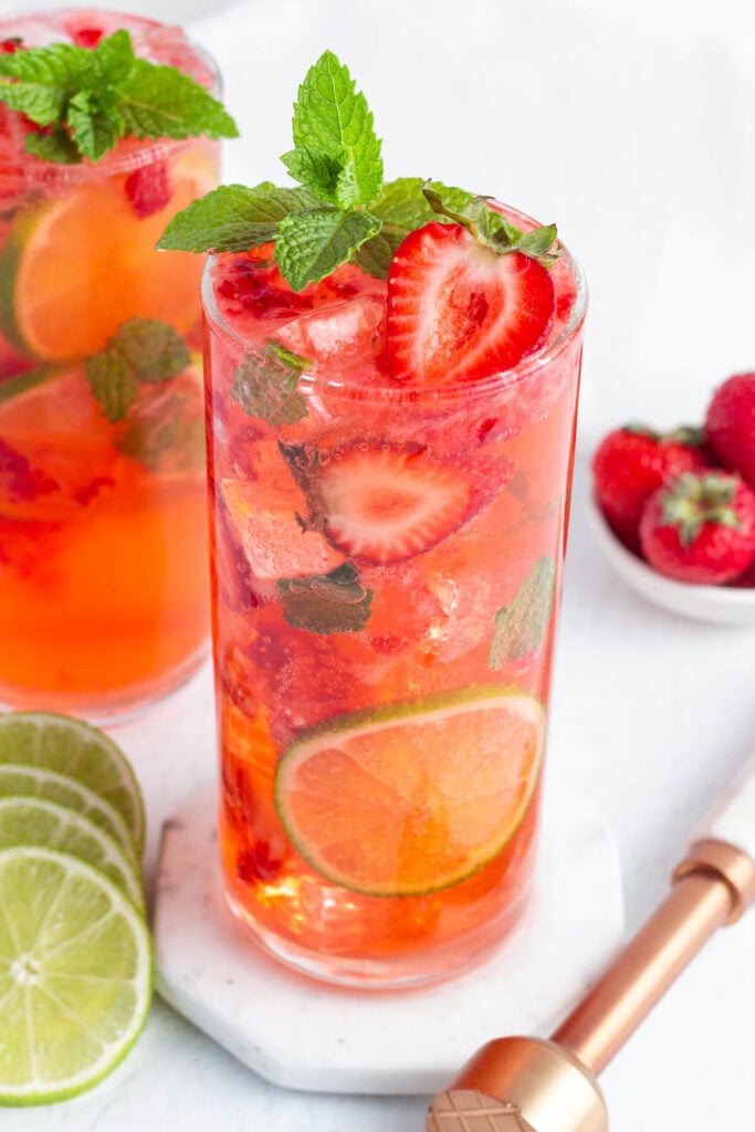 red strawberry mojito mocktail in a tall glass garnished with fresh strawberries, mint and lime rounds.