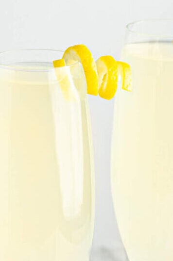 two champagne glasses garnished with a lemon twist on a grey background