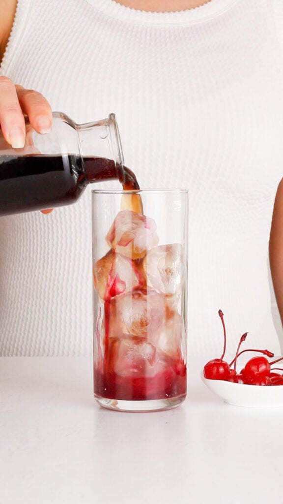 tall ice filled glass with grenadine at the bottom and cola being poured over the top