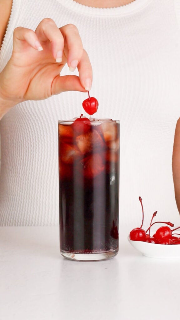 roy rogers mocktail being garnished with a maraschino cherry