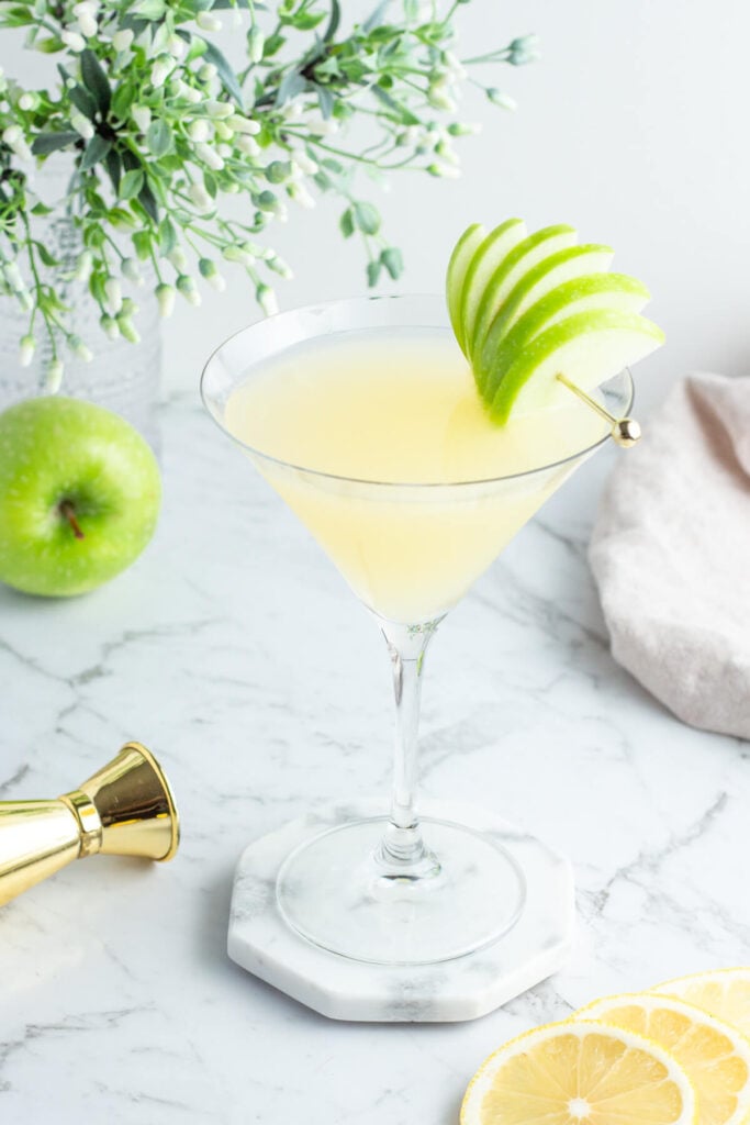 cola de appletini en una copa de martini con una guarnición de abanico de manzana verde sobre un fondo gris