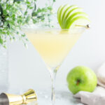 martini glass filled with yellow liquid garnished with a green apple fan