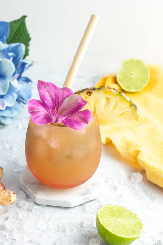 Tropical looking mocktail in a pink coloured glass with a bamboo straw and purple flower as the garnish