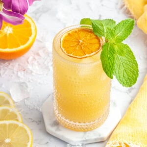 vista de pájaro en una bebida de color naranja parcial que está adornada con menta fresca con rodajas de limón al lado.