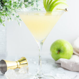 appletini mocktail in a martini glass with a green apple fan garnish on a grey background