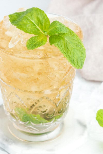 mint julep mocktail drink in a tall glass garnished with a sprig of fresh mint on a grey and white background.