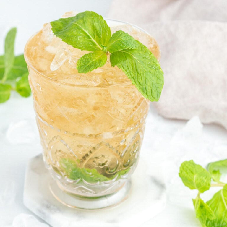 mint julep mocktail drink in a tall glass garnished with a sprig of fresh mint on a grey and white background.