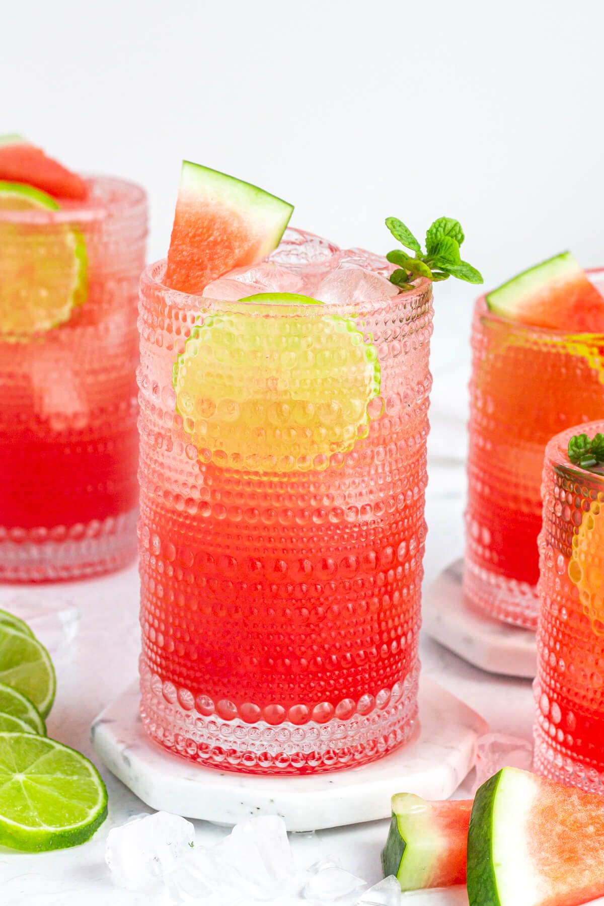 tall clear glass of pink fresca garnished with a lime round, watermelon wedge and mint.