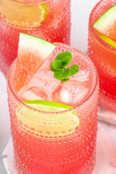 several glass of watermelon fresca garnished with mint, lime and watermelon, with lime rounds in the background.