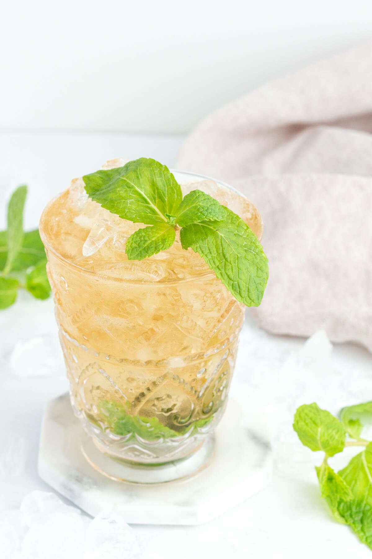 non alcoholic mint julep in a tall clear glass garnished with a mint sprig with mint and ice blocks in the background