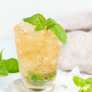 brown drink in tall glass with mint at the bottom, with a mint sprig on top and a white background