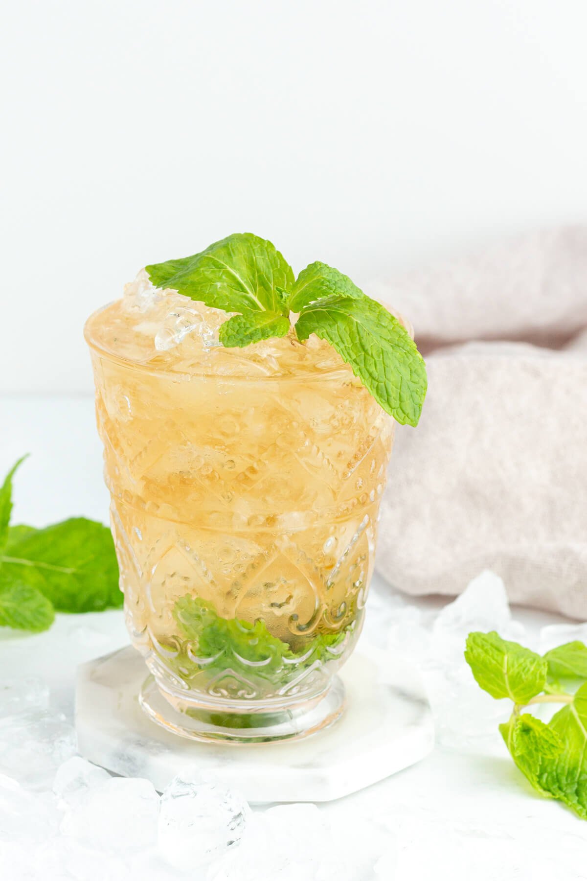 brown drink in tall glass with mint at the bottom, with a mint sprig on top and a white background