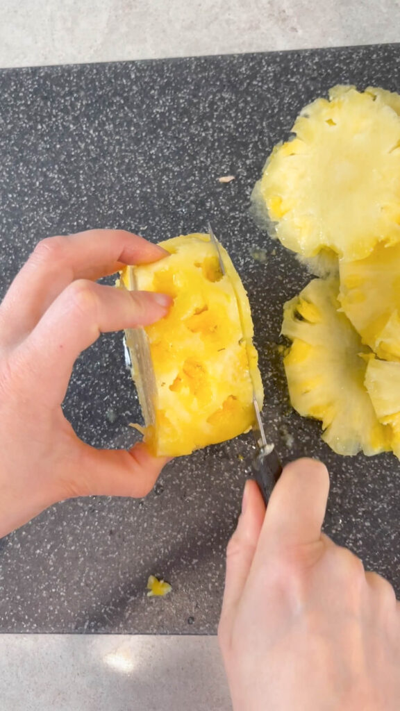 whole peeled pineapple being cut into thin slices to make dried pineapple flowers.