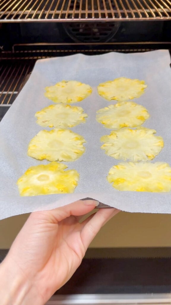tray of 8 thin pineapple slices on a baking tray being placed into an oven.