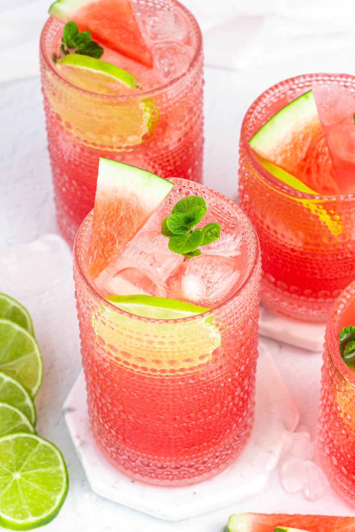 three tall glasses of pink watermelon agua fresca garnished with mint, lime rounds and watermelon wedges.