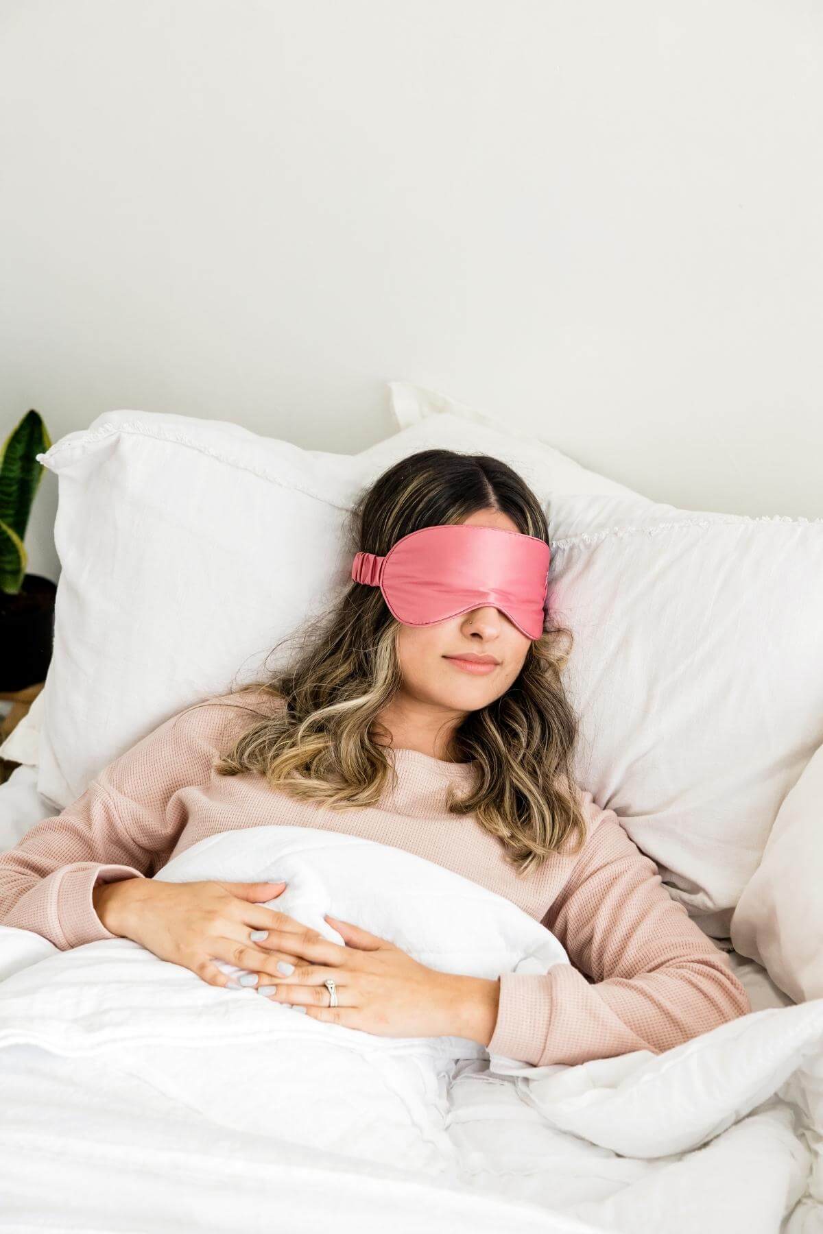 woman sleeping in bed with a pink satin eye mask over her eyes.