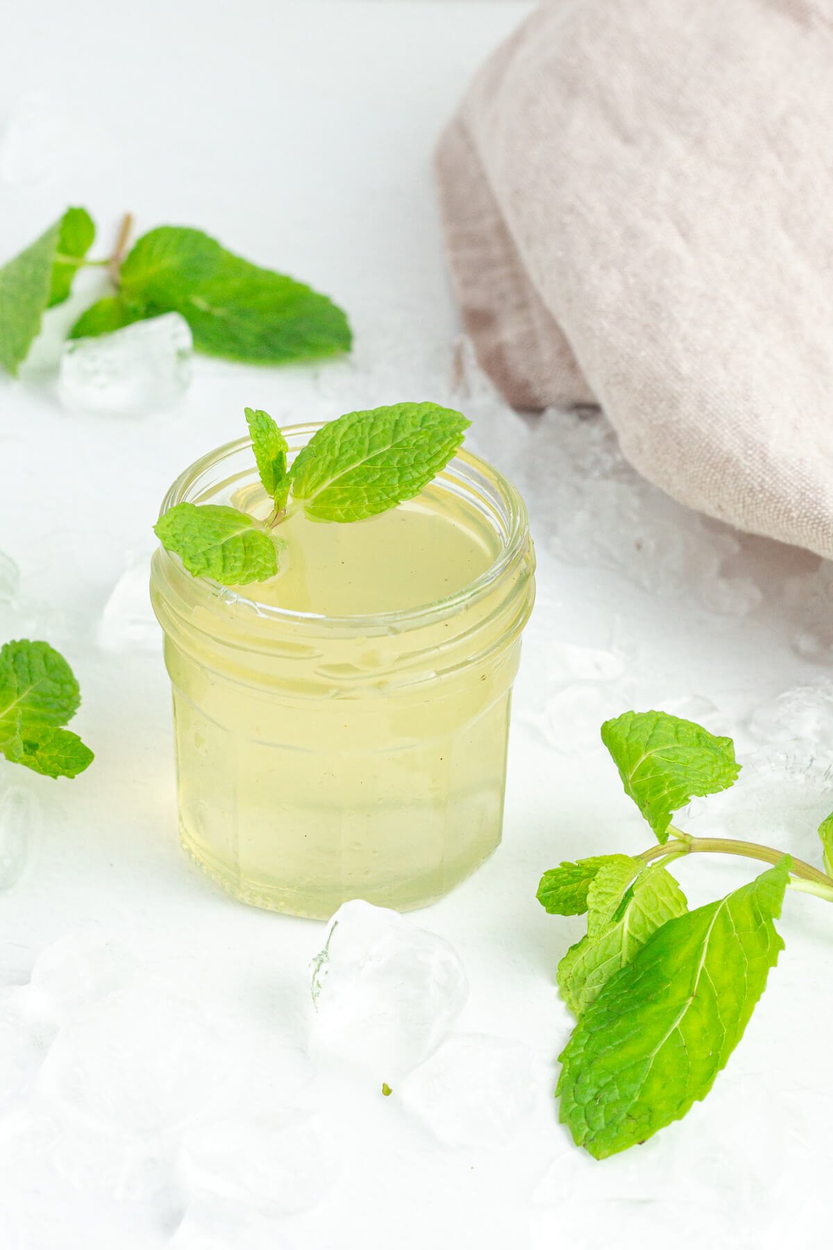 small glass pot of mint simple syrup garnished with fresh mint and fresh mint and iceblocks scattered around.