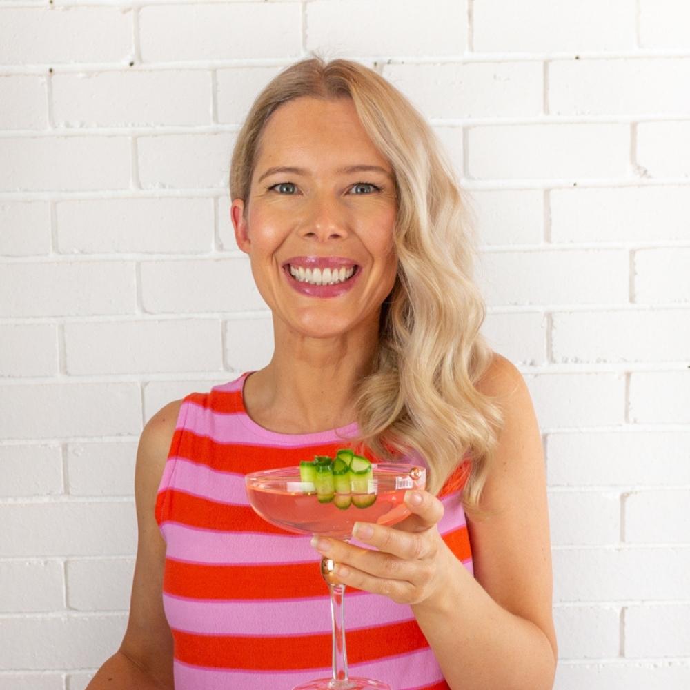 blonde woman in a pink and red top holding a mocktail.