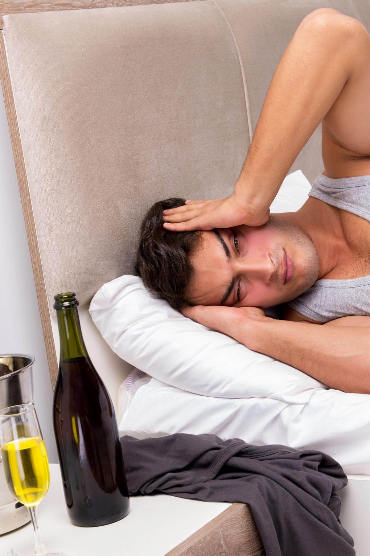 man lying in bed unable to sleep with a bottle of wine and glass next to his bed.
