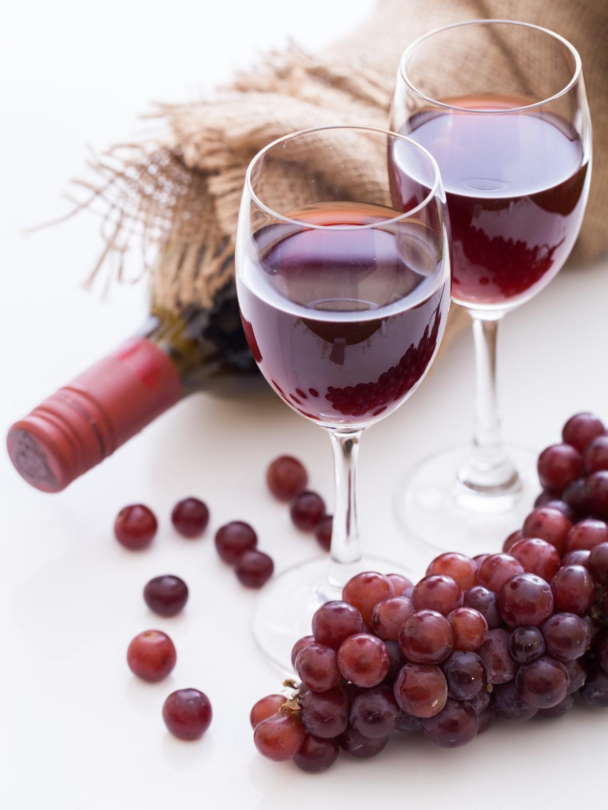 two glasses of red wine with red grapes nearby on a cream background.