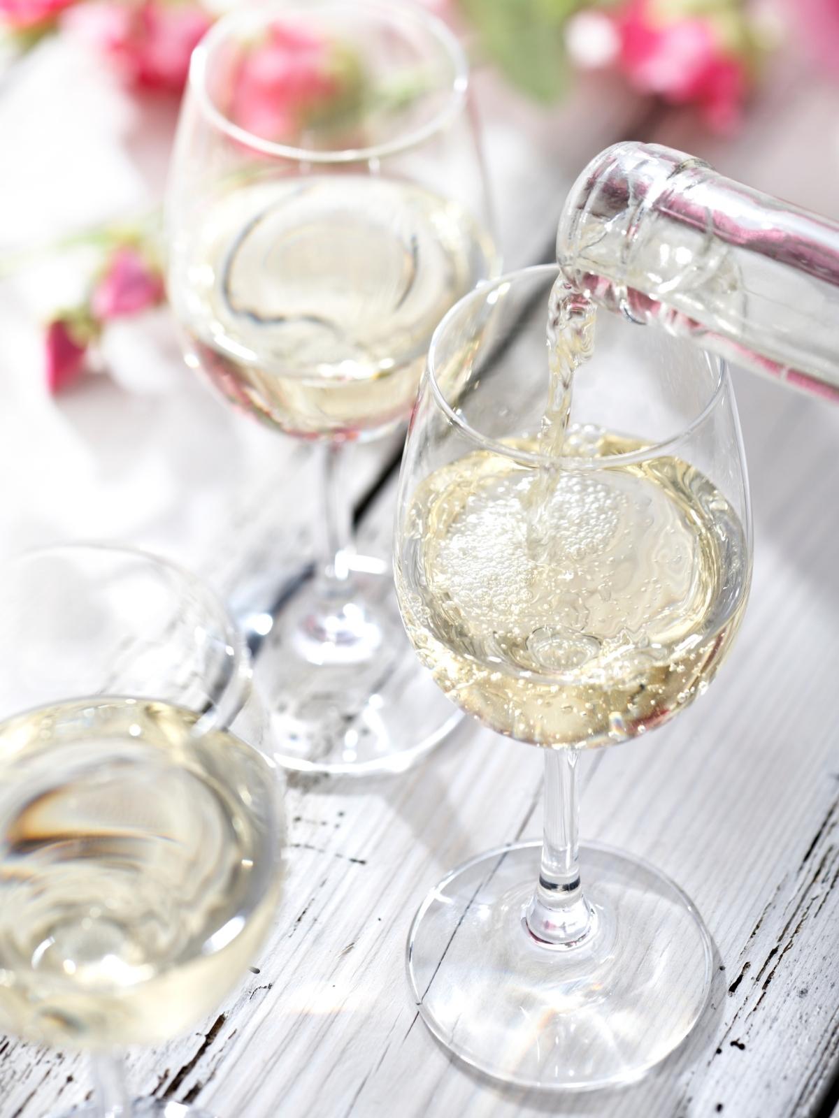 two glasses of crisp looking white wine on a white tablecloth with pink flowers in the background.