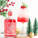red and white festive mocktail in a wine glass garnished with rosemary and 3 cranberries, with a bottle of Lyre's Italian Orange next to it.