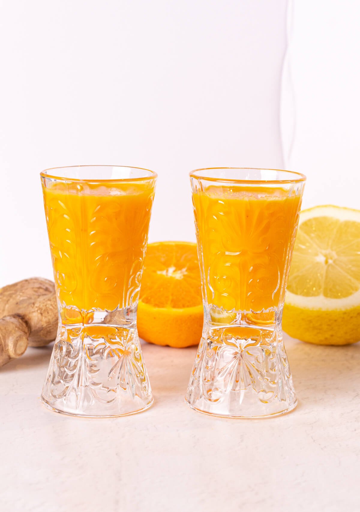 two wellness shots made with ginger turmeric and orange in glass shot glasses on a white background.