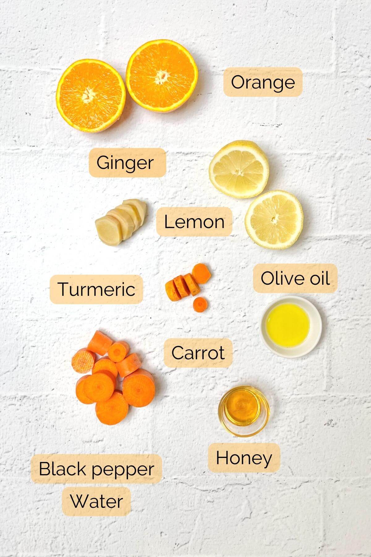A flat lay of wellness shot ingredients including ginger turmeric orange honey carrot and olive oil.